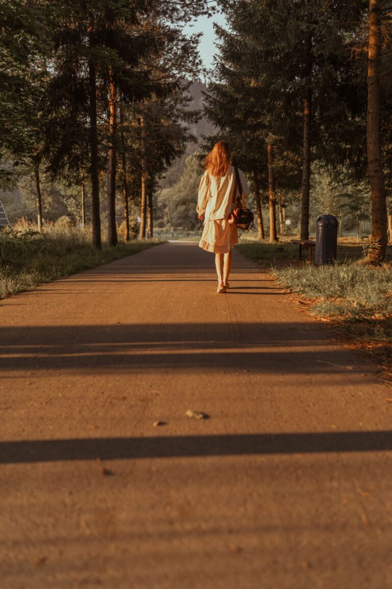 Woman walking away down a tree-lined path in golden evening light