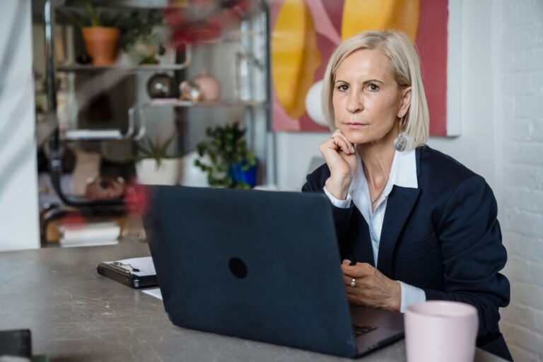 Blonde woman pausing in thought at a desk with a laptop