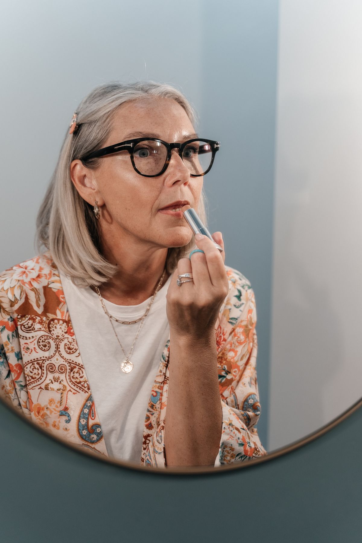 Woman with a grey bob looking at her reflection while applying lipstick