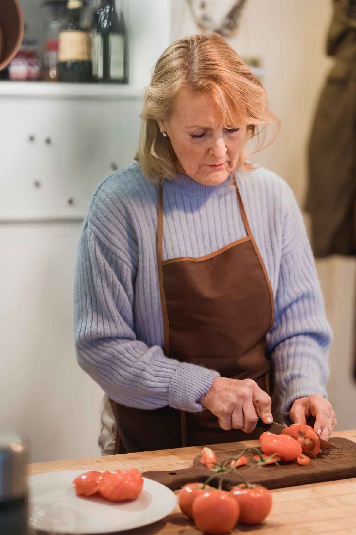 Woman in an apron slicing tomatoes at a kitchen counter