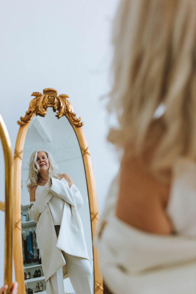 Silver-haired woman smiling at her reflection in an ornate mirror