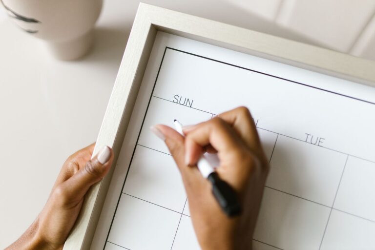 A hand marking a date on a monthly wall calendar