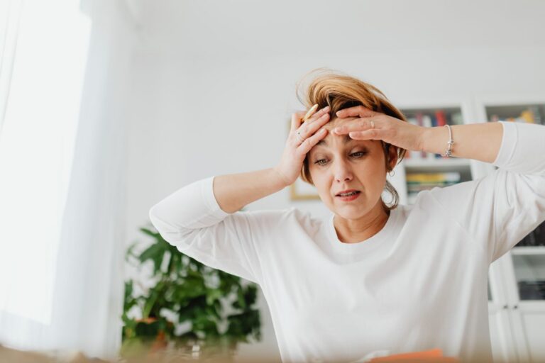 Woman at a desk pressing her hands to her head in frustration