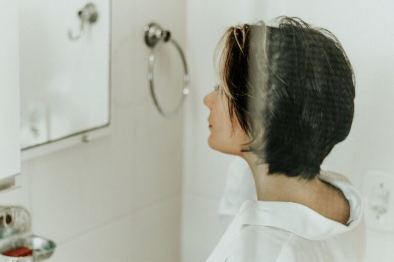 A woman with short dark hair looking at herself in a bathroom mirror