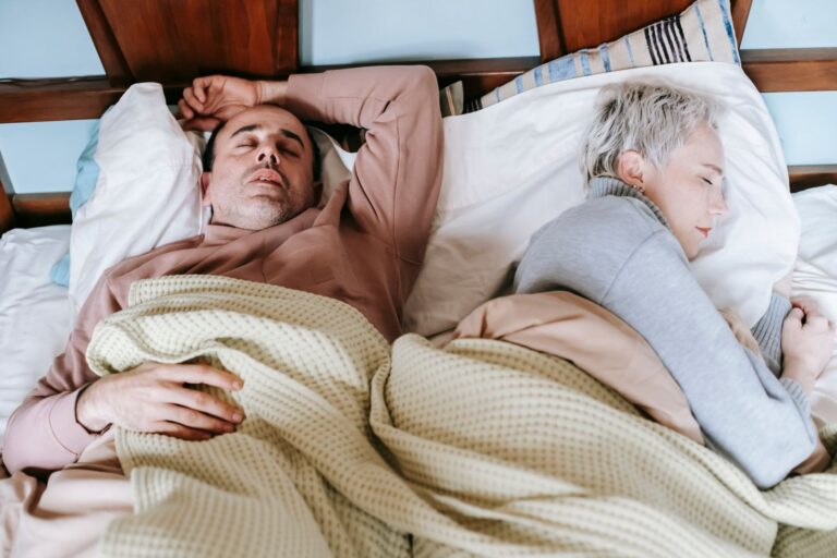 A middle-aged couple lying in bed, the woman turned away and the man awake