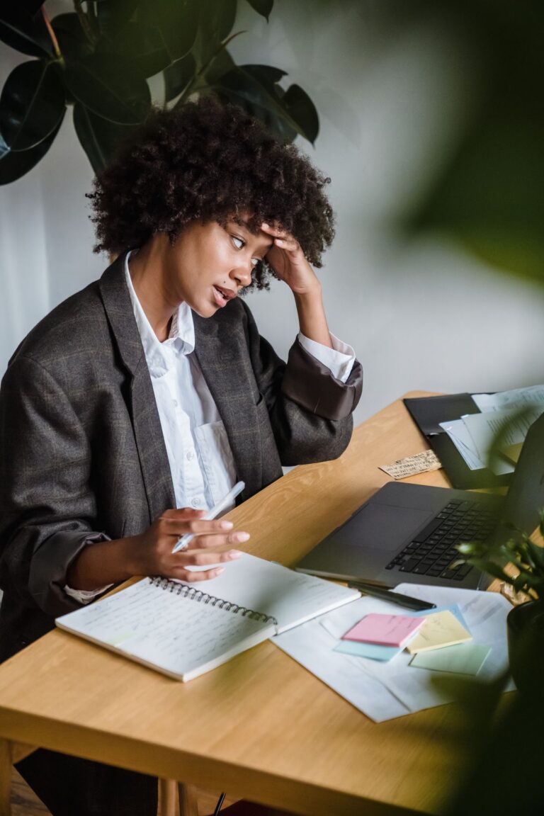 Woman at a laptop resting her forehead on her hand, sticky notes on the desk