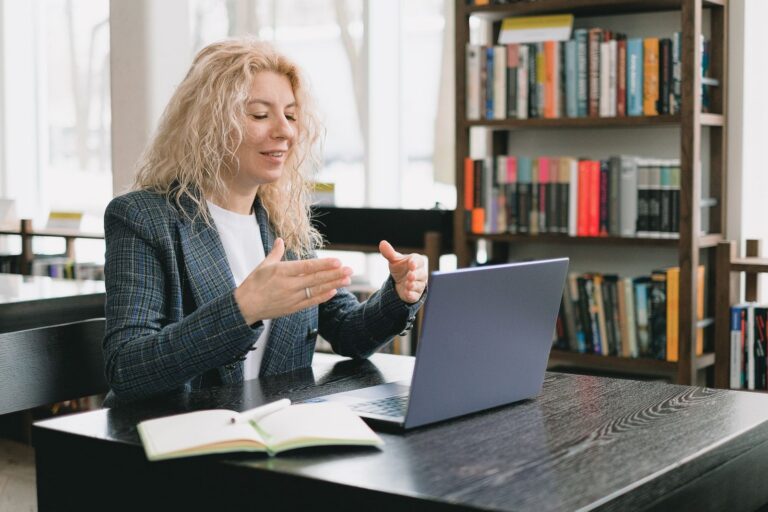 A woman in a blazer talking on a video call at her laptop in an office