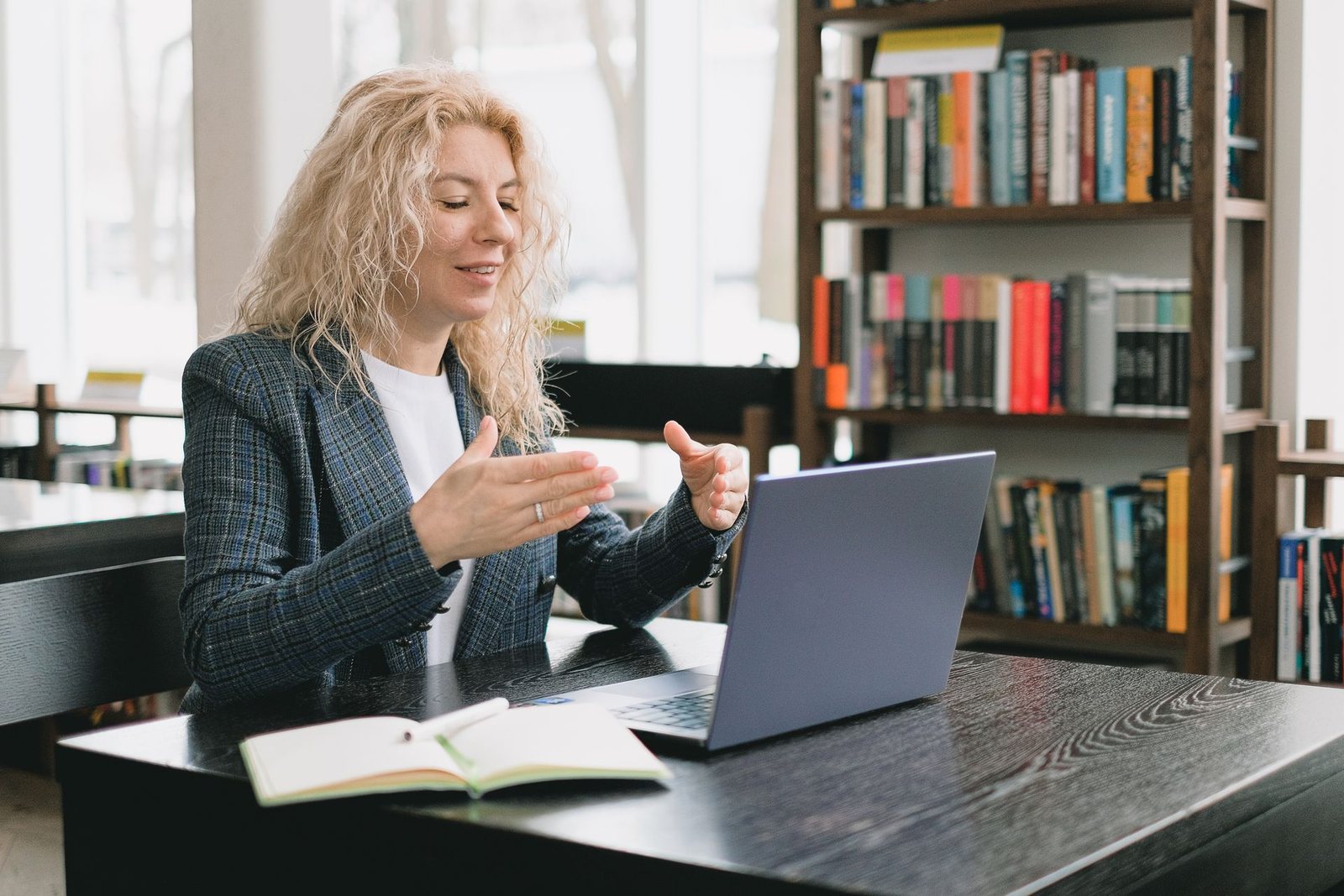 A woman in a blazer talking on a video call at her laptop in an office