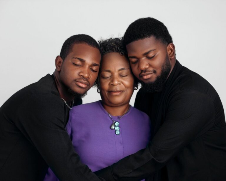 A mother with her eyes closed being hugged by her two adult sons