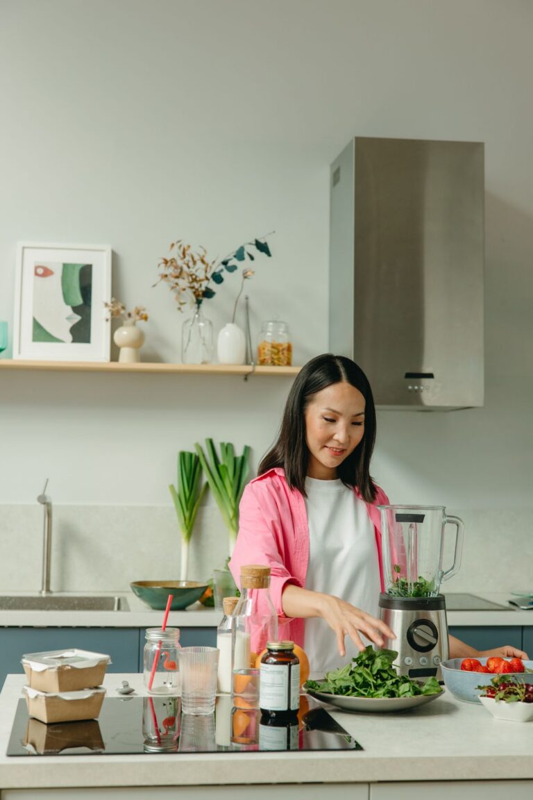 Woman adding spinach to a blender in a bright kitchen
