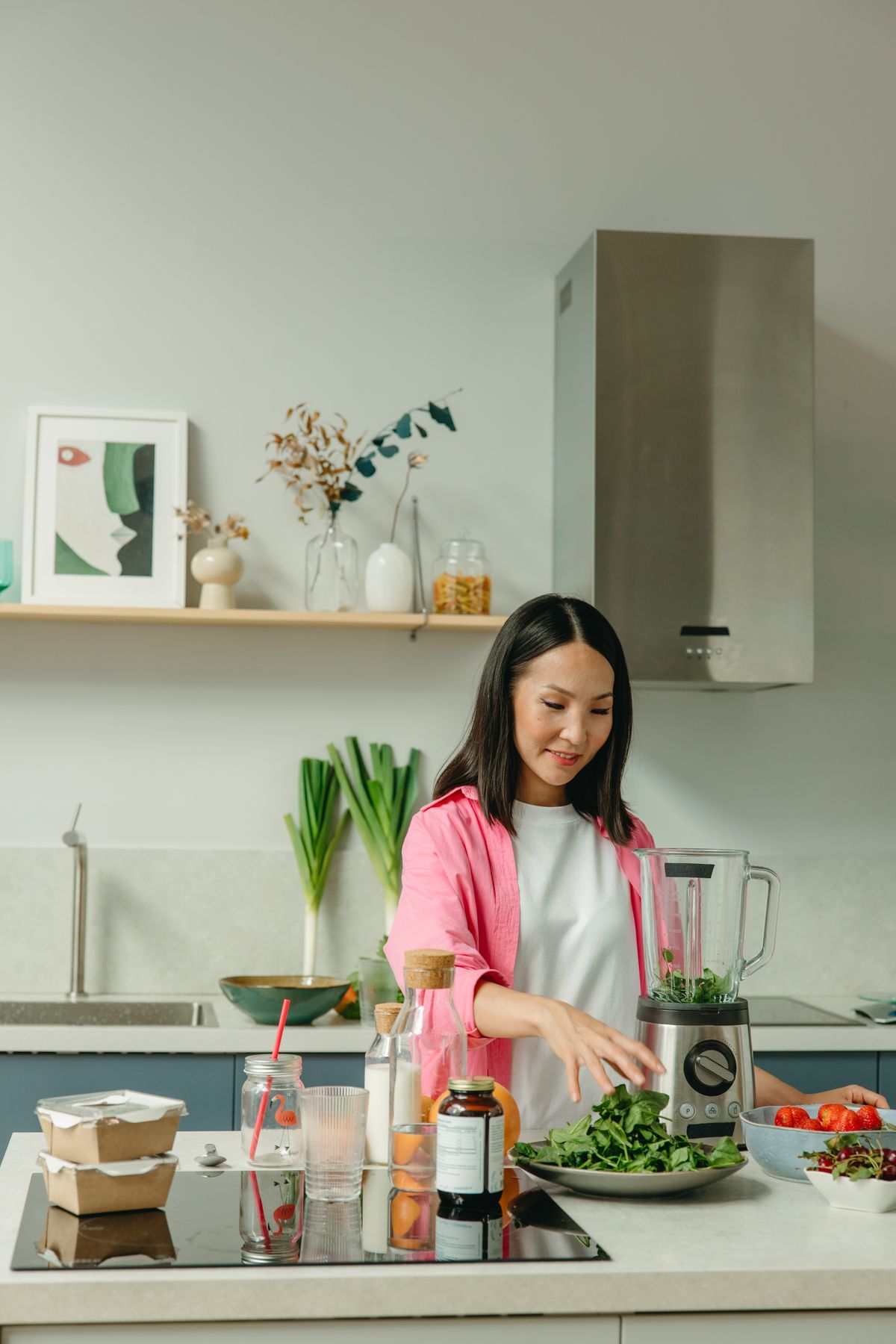 Woman adding spinach to a blender in a bright kitchen