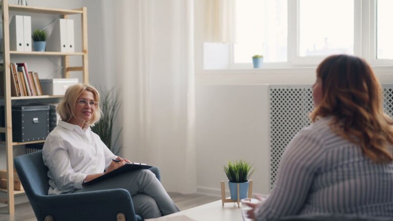 A counsellor with a notepad listening to a client in a bright consulting room