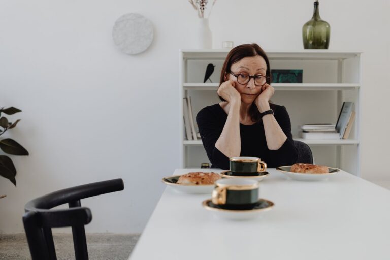 A woman in her fifties sitting at a table with coffee, chin resting on her hands